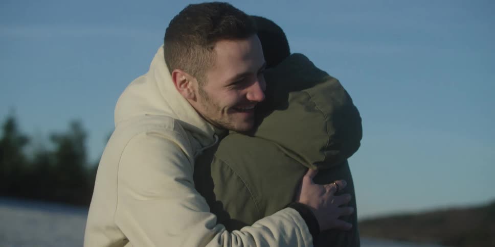 Man hugging another person outdoors during the daytime both wearing jackets