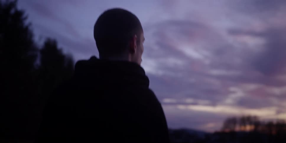 A young man wearing a hoodie walking outdoors spinning around as he appears confused