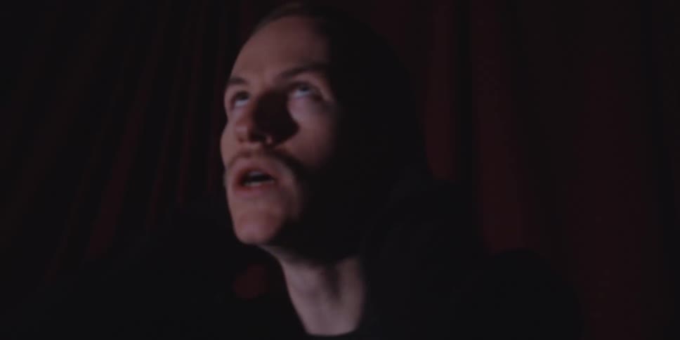 A distressed man clutches his head with both hands in a dimly lit room