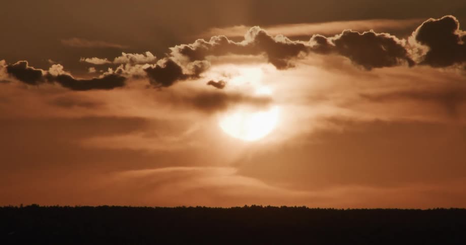 Sun setting behind dense clouds above a dark horizon line