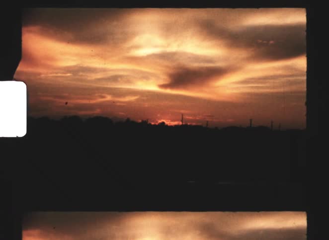 A dramatic orange sunset spreads across the sky above a dark horizon