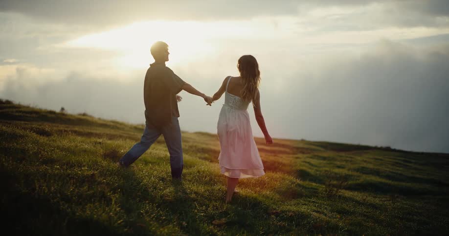 The couple are holding hands as they walk barefoot on the grass