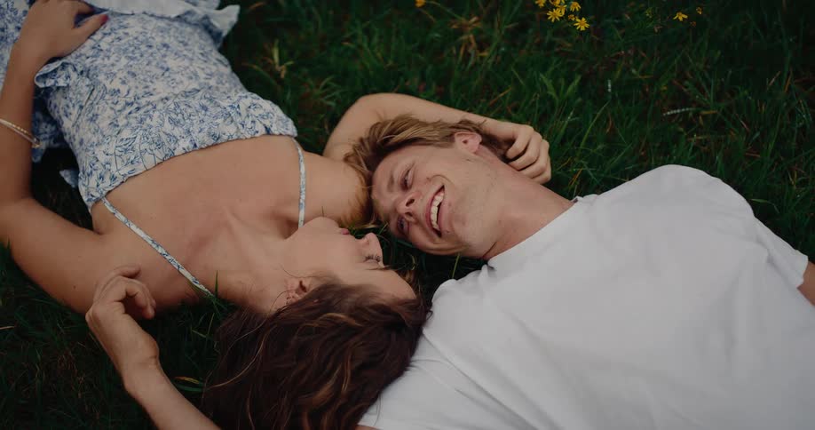 Couple lying on grass looking at each other in an outdoor area