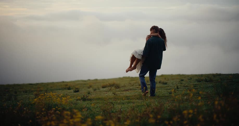 Couple in an open field with one person carrying the other under an overcast sky