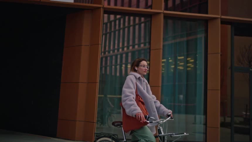 Woman rides her bicycle on the sidewalk in front of buildings as she stops to look around