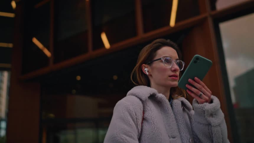 Woman standing outside of a building holding her phone and pressing buttons with her finger