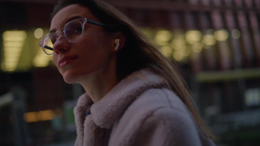 A young woman walks in a large city while texting on her smartphone at dusk