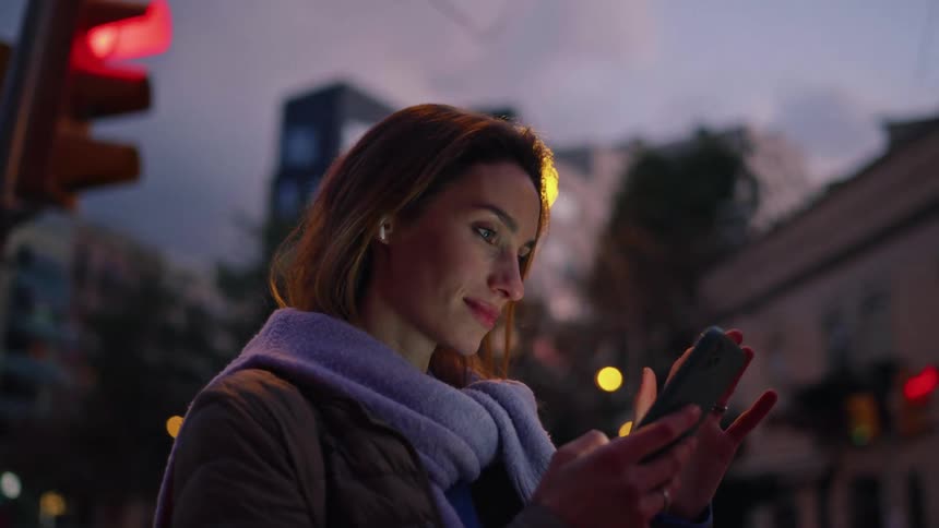 A woman stands outside and smiles while viewing her phone