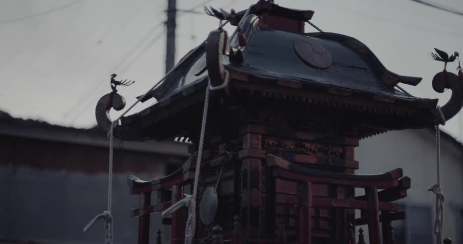 During a street festival under a gray sky a detailed traditional shrine sways rhythmically as it is carried through the town