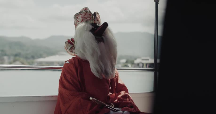 Person wearing traditional red clothing seated on a boat looking toward a mountainous landscape