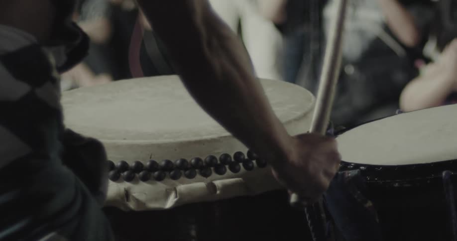 Extended arm strikes traditional drum in nighttime performance
