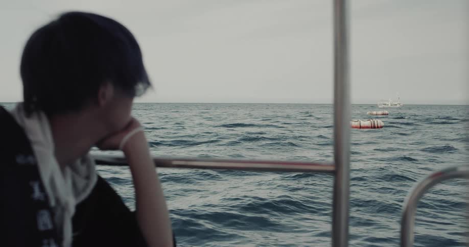 Person leaning on railing watching the sea with floating buoys in the background