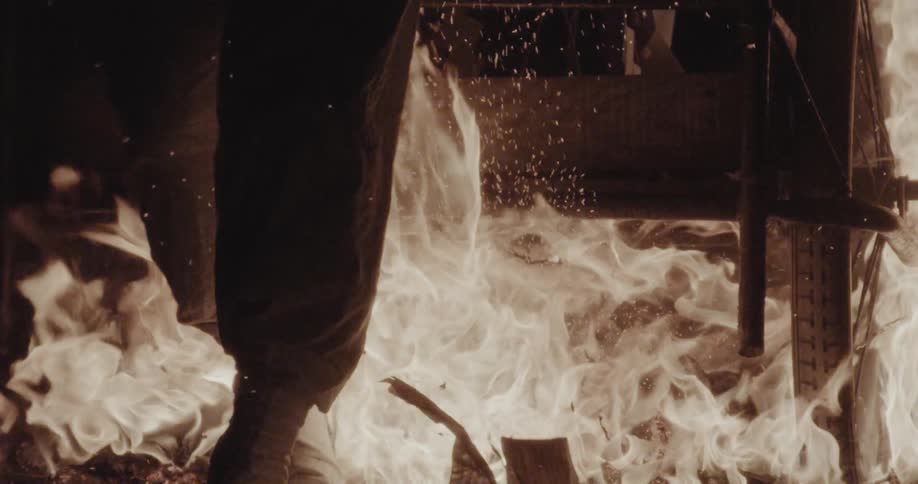 A large burst of orange fire and then the silhouette of a persons legs passing over it