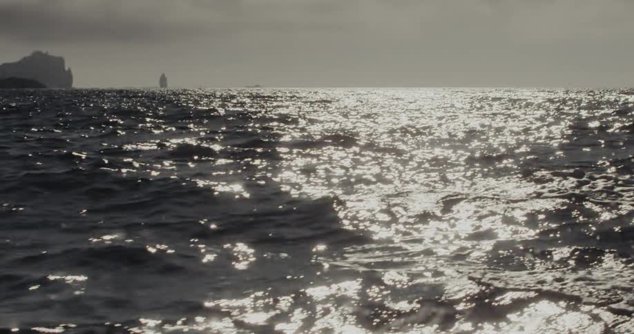 Sea surface with light reflections under a cloudy sky and rocky silhouettes in the background