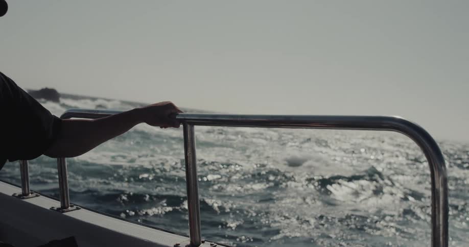 Hand resting on a metal support of a boat moving at sea