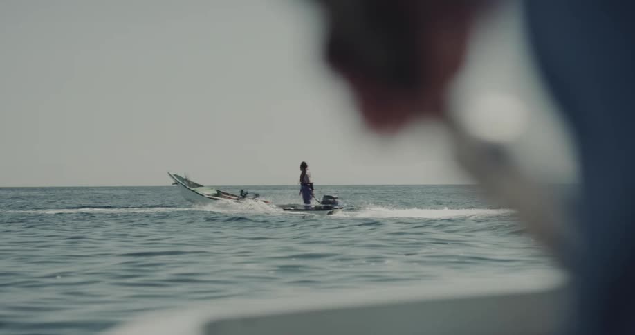 View from a small boat of waves rolling in to shore as a person standing on another boat passes by