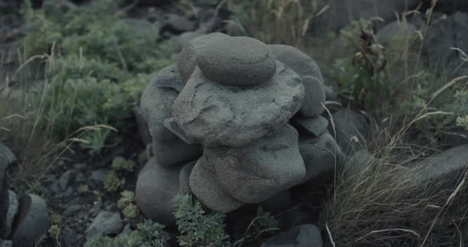 A series of small rocks stacked on top of one another in a grassfield with short grasses swaying gently in the wind