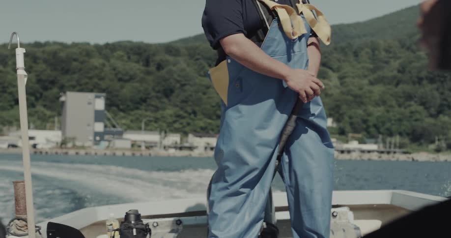 Person works on boat with view of forested coast
