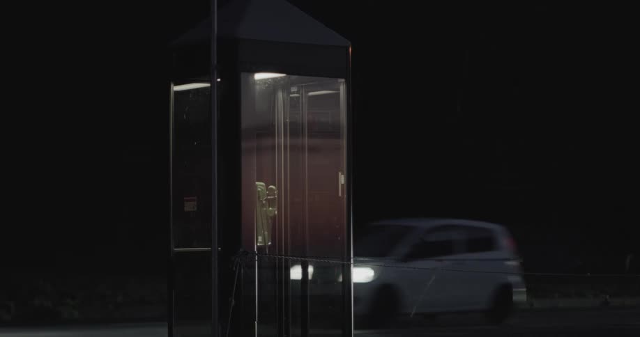 The car drives by the phone booth at night