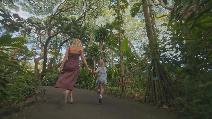 A child running to her mother and the two of them holding hands as they walk along a woodland path at midday enjoying their time together
