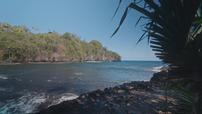 A rocky coastline at midday with waves crashing rhythmically against the rugged shoreline under the bright sun
