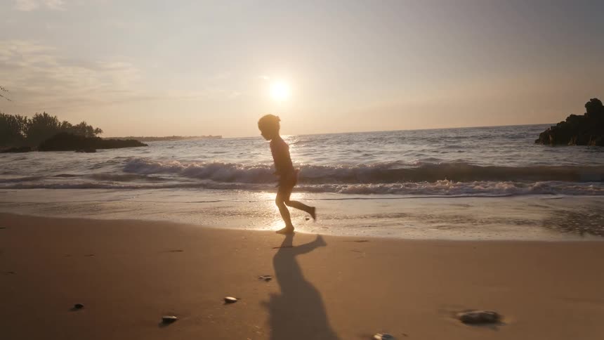 Little girl running and playing on the beach as waves roll in to shore
