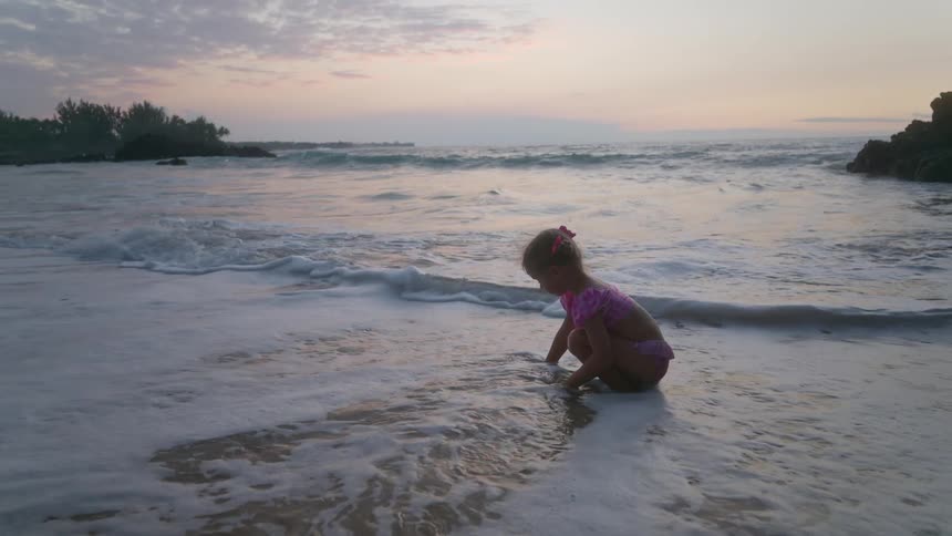 The little girl plays in the water of the beach