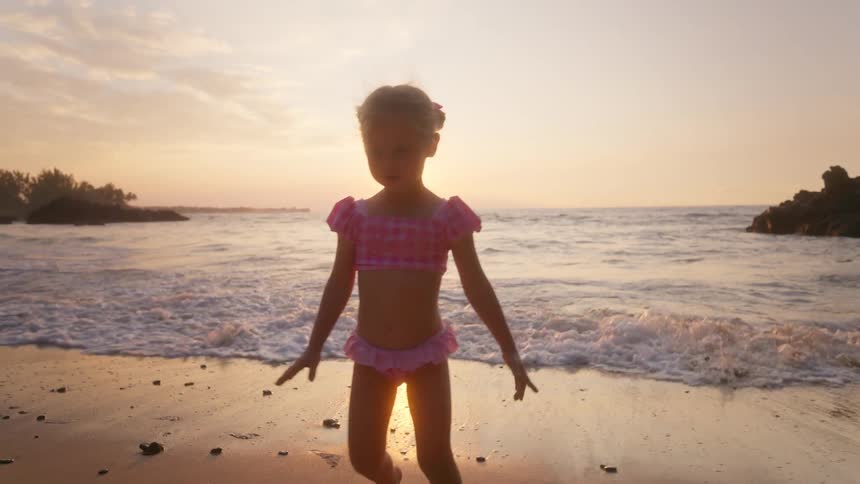 Little girl playing on the beach walking in the water as waves roll in to shore