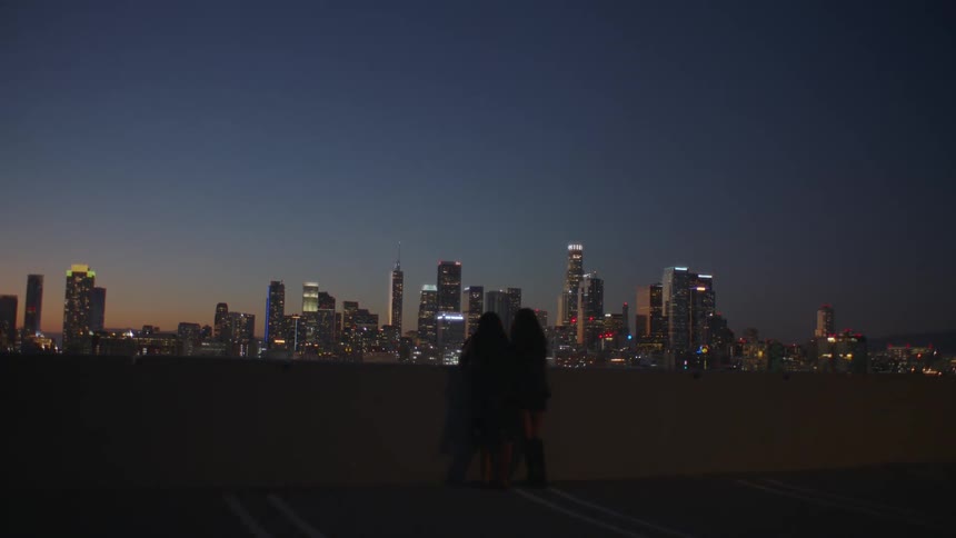 Two young woman standing on the top floor of a parking garage with a view of the metropolitan skyline in the distance
