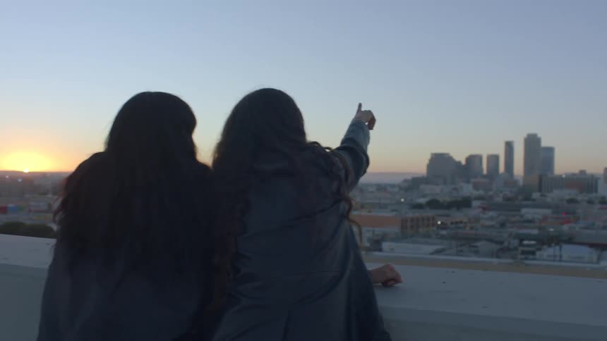 People observe urban horizon at sunset from rooftop