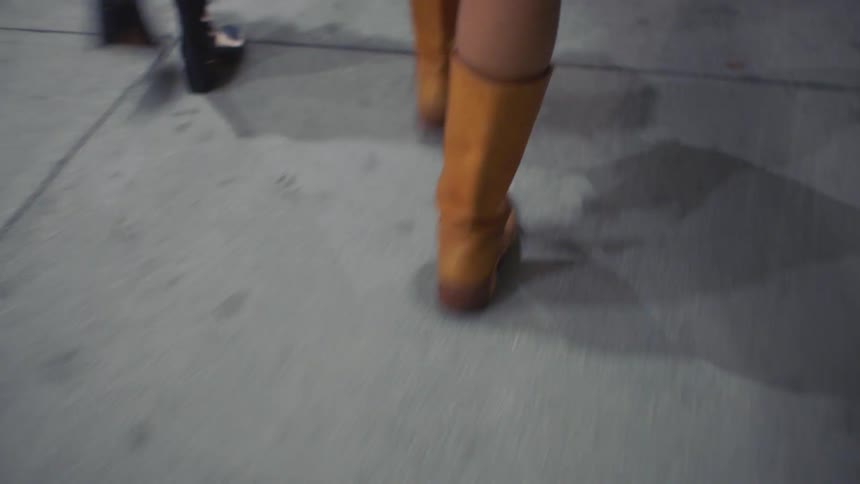Orange boots stand out in firm stride on concrete sidewalk