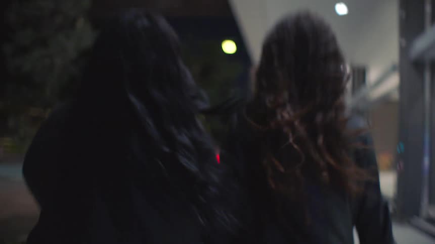 Two friends walk on the sidewalk at night
