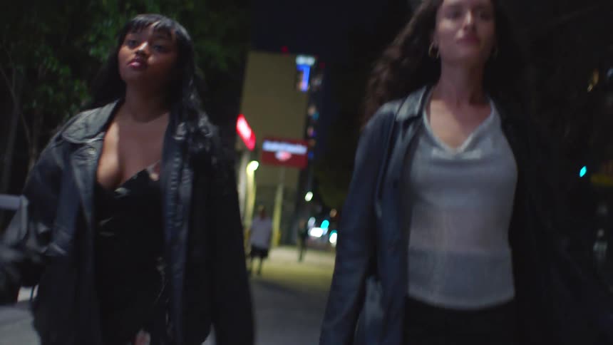 Women walking side by side on an urban street at night