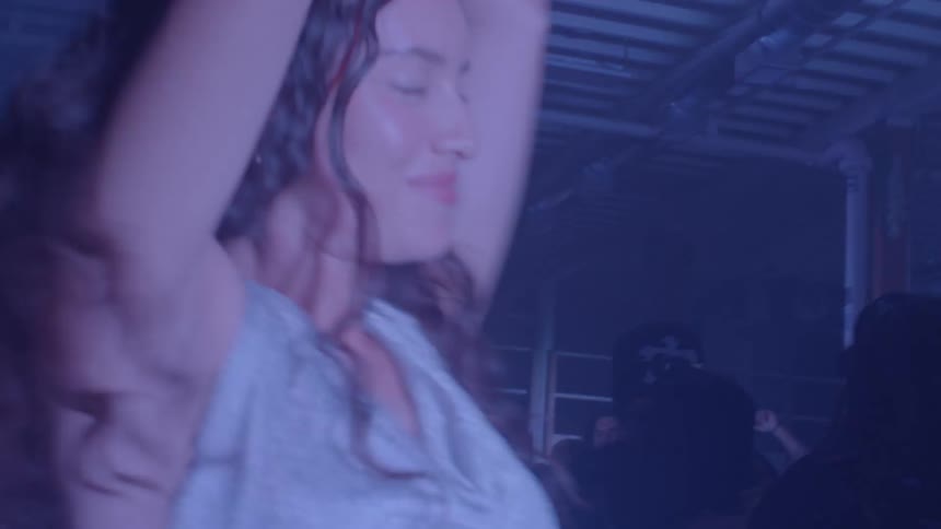 In a dimly lit nightclub a woman dances with her hands in the air her silhouette moving as the lights flash from an intense blue to a pulsing red