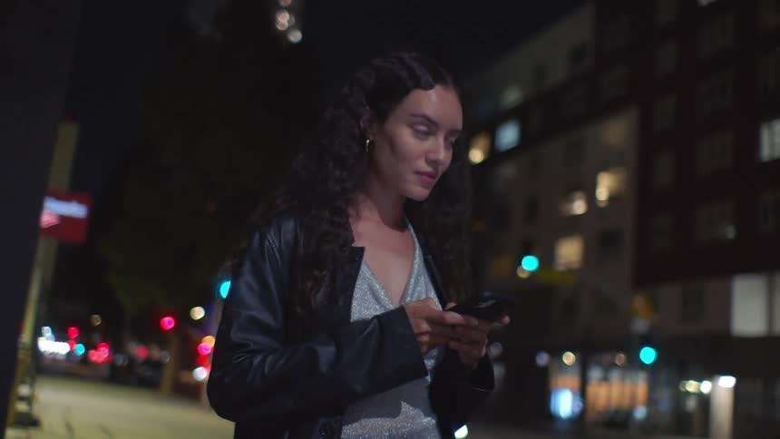 Curlyhaired woman checks phone on urban street at night