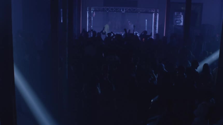 Crowd gathered in an indoor venue with stage lighting and people raising their arms