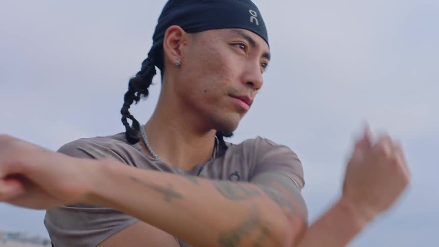 A young hispanic man with tattoos across his arm stretching outdoors