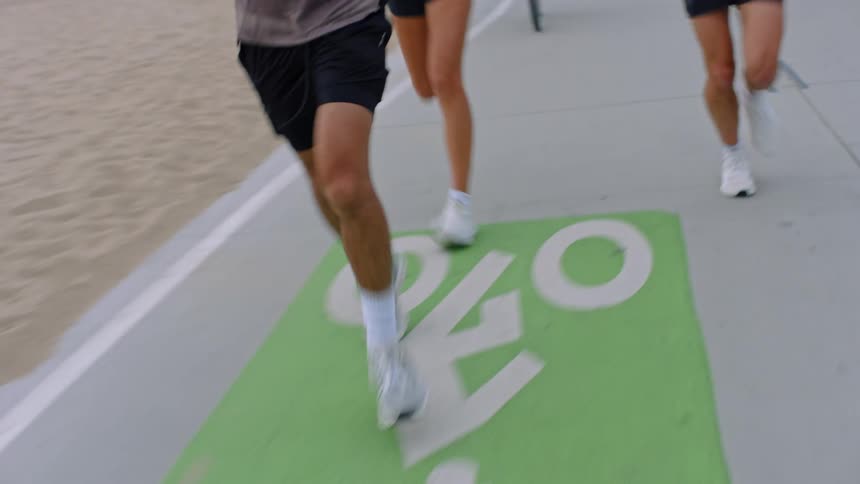 Legs of three people running outdoors along the edge of the beach sand