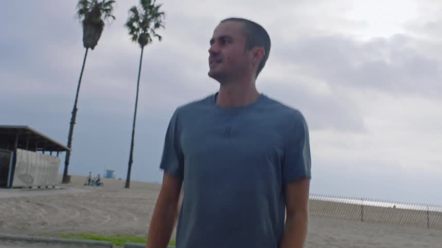 A man smiles while stretching his arms before setting off on a jog along a beachside path under an overcast sky