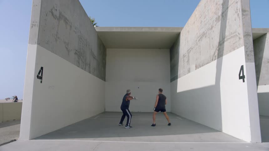Two men playing handball on a handball court on a sunny day