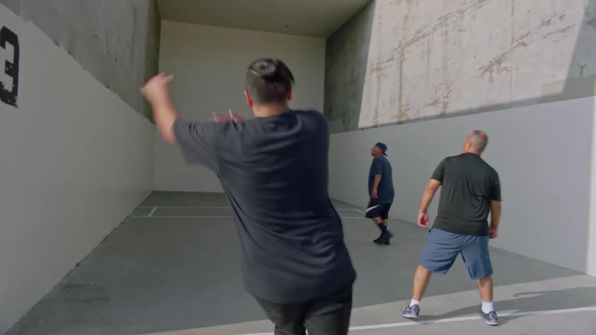 Four men in black shirts are playing a sport of hitting balls against a wall