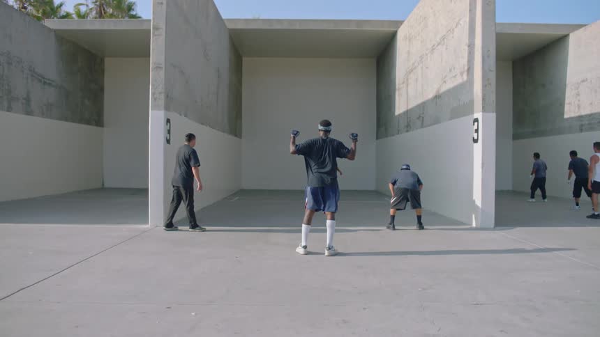 Three men with their backs turned are looking at a tall white wall with two enormous walls on either side