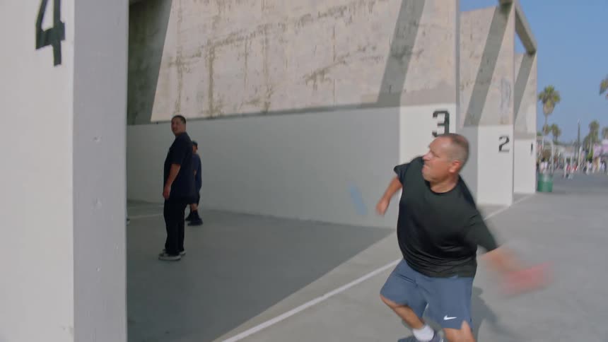 Man runs backward to return a ball during a game of handball on a summer day