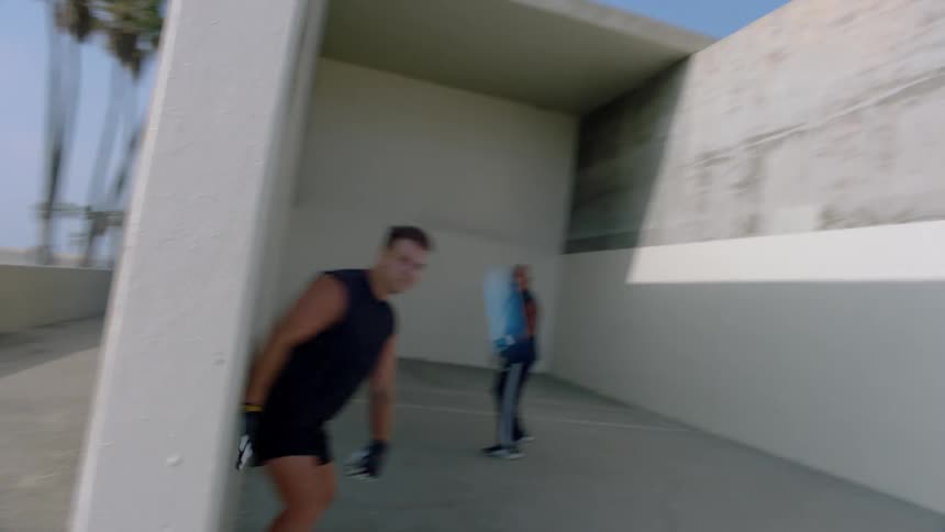 Two men practicing sports with a small ball in a space surrounded by white walls