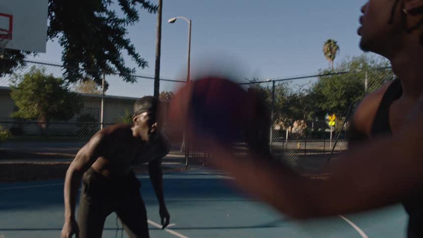 Two young black male athletes playing basketball at an outdoor court in a suburban city during daytime