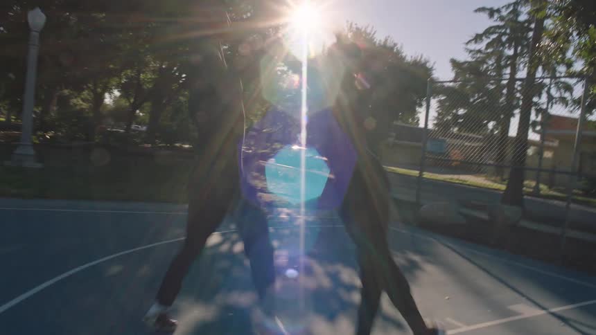 Two men are playing basketball on an outdoor court and one of them is throwing the ball to the hoop