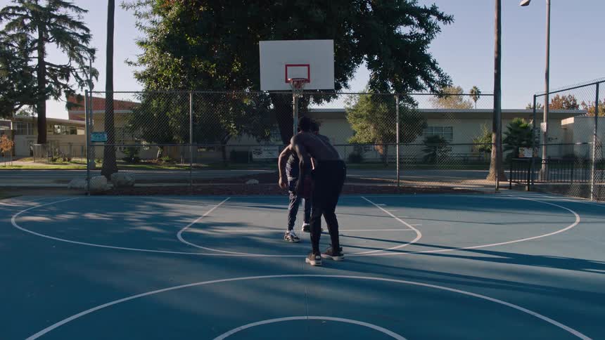 Two men are playing basketball on a court with a blue floor and one of them is shooting the ball into the basket