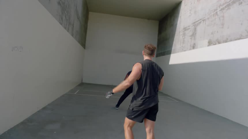 Two men throwing a small ball against a white wall