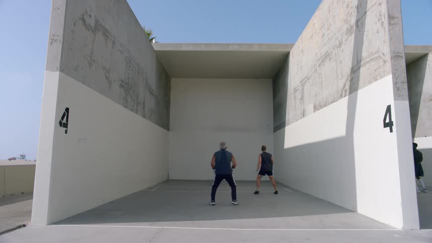 Men throwing a small ball against a white wall during a sporting practice