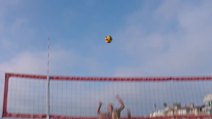 A group of four young women play volleyball on the beach